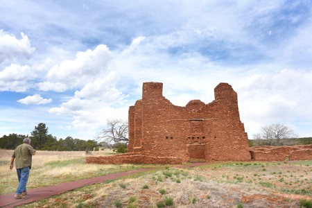 Man walks path toward the ruins of the Quarai Mission and Convento, at the Salinas Pueblo National Monument, in New Mexico.  Red Sandstone mission is in front.の写真素材