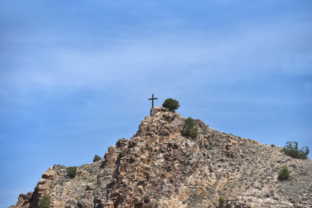 Rustic cross sits on top of rocky mountain top at Cerrillos, New Mexico.  Blue sky fills background.の写真素材