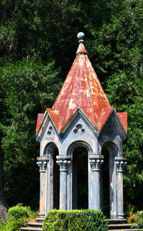 Castle-like gazebo is ornate with rustic tin roof.  Ball shaped finial tops roof.  Grey, decorative...