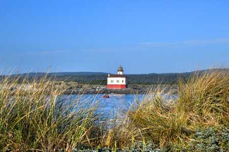 Fishermen enjoy view of the Coquille River Lighthouse, near Bandon, Oregon.  Their red boat floats directly in front of historic lighthouse.の写真素材