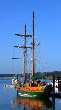 Wooden brigatine sits in Bandon Harbor, in Oregon.  It has green trim.  Blue water reflects docked...