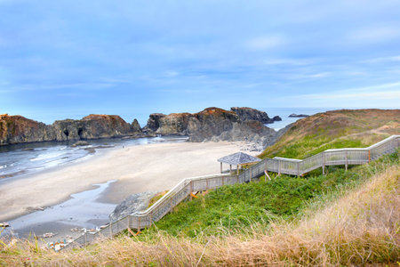 One person stands on Bandon Beach in Oregon.  Beach is otherwise deserted.  View can be seen of Elephant Rock and offshore islands.  Wooden steps descend to beach.の写真素材