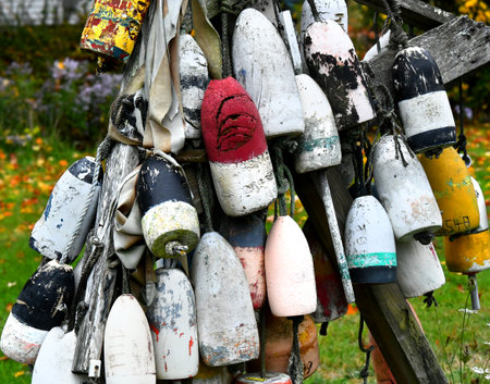 Collection of weathered and faded fishing floats hang from a rustic wooden frame.  Floats are in...