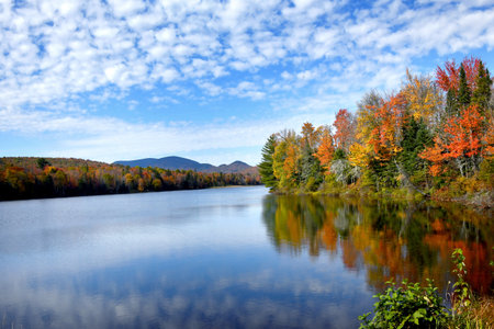 Fall colors are reflected on the surface of the Pontook Reservoir, in New Hampshire.  Distant views of the White Mountains can be seen.の写真素材