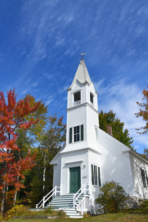 Saint Johns United Methodist Church, in Jefferson, New Hampshire, is a white, wooden structure with bell tower.  Blue sky and Fall foliage surround it.の写真素材