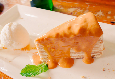 A peice of Thai tea crepe cake served with a scoop of vanilla ice cream garnihed with mint leafの写真素材