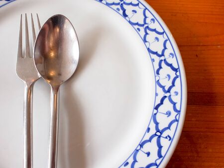 An empty plate with spoon and fork on wooden background