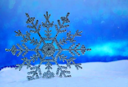 Big shiny snowflake in the snow and blue sky from behind. Blurred background. Merry Christmas card. New year bokeh. Copy spaceの写真素材