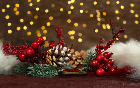 Spruce branches with red berries and pine cones on a red Santa Claus' hat with new year lights in the back. Blurred background. Christmas cardの写真素材