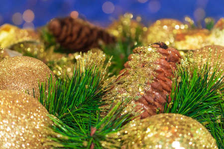 Shiny yellow Christmas balls and cone with barks and pine branches. Blue background with bokeh. New year card. Copy spaceの写真素材