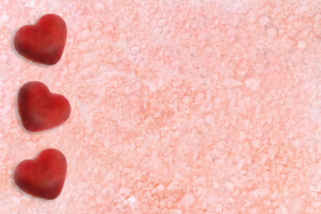 Beige pink background with three hearts on the side. Sea salt. Texture. spa backdrop. St. Valentine card. Copy spaceの写真素材
