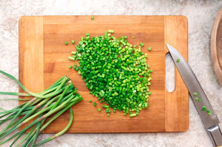 Chopped bunch of green garlic on wooden cutting board with knife.の写真素材