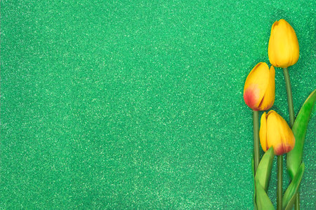 Three yellow tulips on green background with glitter. Greeting card with Easter, March 8, happy birthday, mother's day. Copy spaceの写真素材