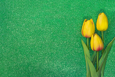 Three yellow tulips on green background with sparkles. Greeting card with Easter, March 8, happy birthday, mother's day. Copy spaceの写真素材