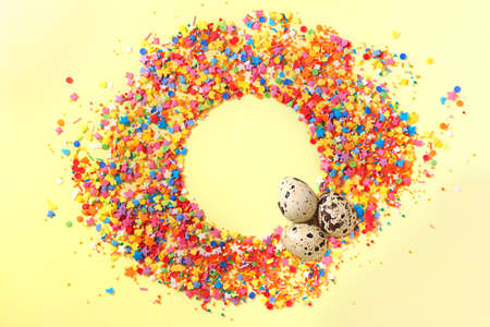 Sweet candy confetti in the middle of a circle with empty space for text and three quail eggs. Yellow backgroundの写真素材