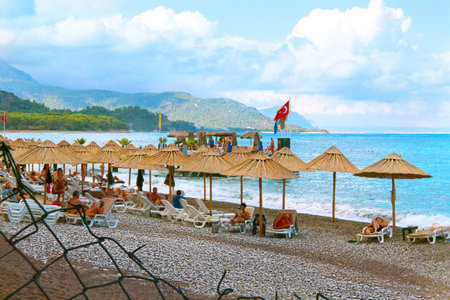 Kemer, Turkey - 09 23 2015: Beach with sun loungers, umbrellas and people. Sea, mountains, palms, pier. Turkey flag. Leisure and travel. Metal fence. Closedのeditorial素材