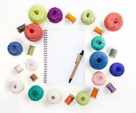 Multicolored balls and bobbins of woolen yarn, wooden thread sleeves on white isolated background. Notepad with pen. Needlework, handmade. view from above. Isolated. Copy spaceの写真素材