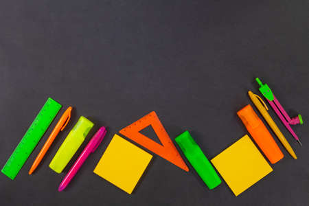 Back to school. Green, yellow, pink, orange office supplies are on the black board, the table. Top view. Rulers, markers, felt tip pens, compasses, pens, adhesive note. Copy spaceの写真素材