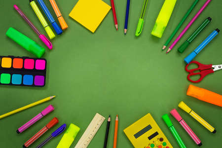 Back to school. Stationery on green background. Markers, pencils, pens, scissors, calculator, ruler, paints, adhesive note. Places for text. Copy spaceの写真素材