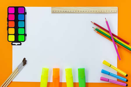Back to school. Education concept. Drawing. Paints, markers, felt tip pens, colored pencils, ruler with white sheet for text on orange background. Copy spaceの写真素材