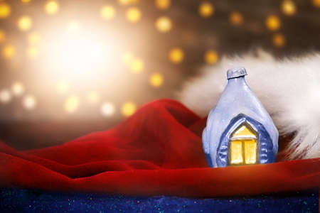 Decorative ice house on Santa Claus's red velvet hat with fur. Blurred lights with lens flare. Christmas, New Year postcard. Copy spaceの写真素材
