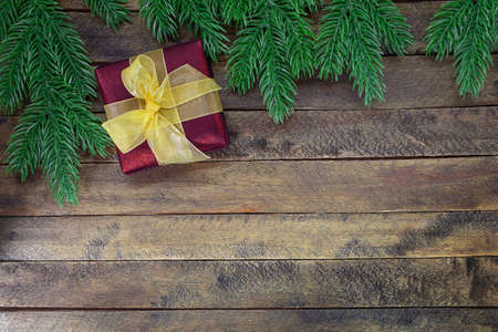 Red gift box with yellow bow on wooden background with Christmas tree branches. New Year. Copy spaceの写真素材
