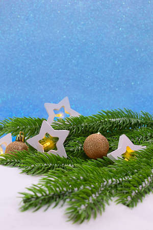 White stars with lights on spruce green branches, with golden balls on snow and blue shiny background. Christmas, New year. Copy spaceの写真素材