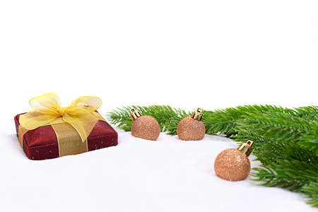 Red gift box with yellow bow and gold sparkling balls, fir branches on snow. white background. Christmas, New Year. Copy spaceの写真素材