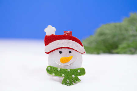 Snowman with a red cap and a green scarf on a snowy background and green trees. Christmas, New Year. Copy spaceの写真素材