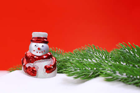 Snowman in the snow and green spruce branches on red background. Christmas, New Year. Copy spaceの写真素材