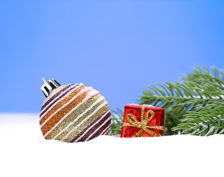 Christmas striped shiny ball with small red gift box on the snow and fir branches. New Year. Copy spaceの写真素材