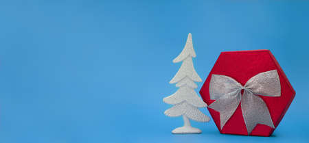 Big red box with silver bow and shiny Christmas tree on blue background. New Year. Copy spaceの写真素材