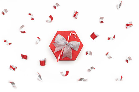 Festive red shiny gift box with silver bow and candy cane confetti isolated on white background. Christmas, New Year, surprise. Copy spaceの写真素材