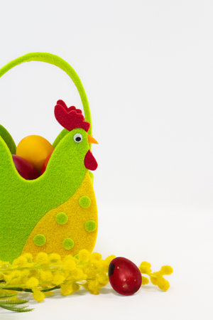 Felt rooster basket with painted eggs and mimosa flowers on white background. Easter. copy spaceの写真素材