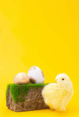 Chicken next to stone pedestal with grass and painted gold and white eggs on yellow background. Easter. copy spaceの写真素材