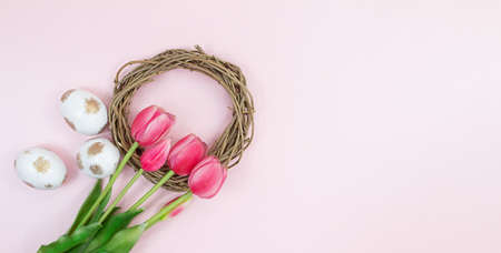 Bouquet of pink tulips with wreath, nest and white eggs with gold on pink background. Easter. copy spaceの写真素材