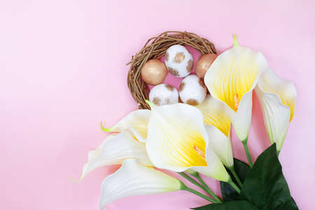 Bouquet of white yellow callas with nest with painted white and golden eggs on pink background. happy easter. copy spaceの写真素材