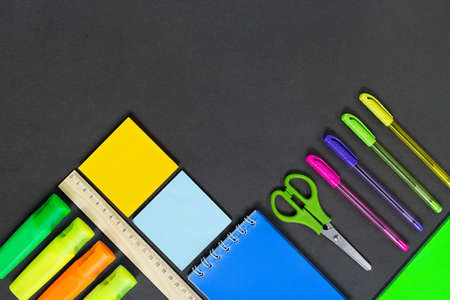 Stationery on black background or school board. Markers, pens, notepad, scissors, ruler with place...