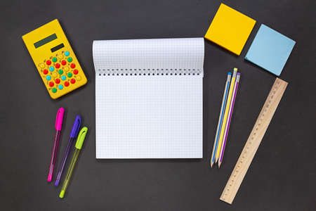Notepad, yellow calculator, pens and pencils, stickers, ruler on a black background. Stationery for...