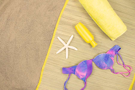 Straw sunbed with swimsuit, towel, sunblock, starfish on sand. view from above. Concept of...