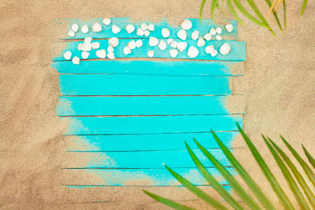Turquoise boards with seashells on beach sand and palm tree. vacation, travel concept. copy space