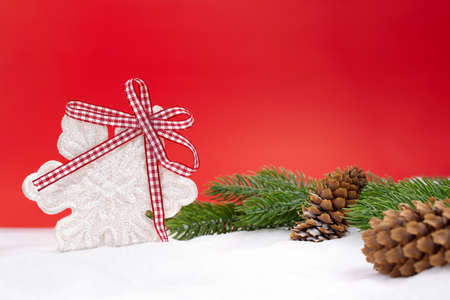 White shiny snowflake with bow, fir branches and cones on snow, red background behind. Christmas, New Year, winter. copy spaceの写真素材