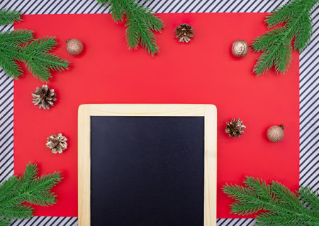 Black chalk board for announcement with spruce branches, golden cones and walnuts, glitter balls on red background and striped. Christmas, New Year flat lay. copy spaceの写真素材