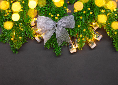 Silver bow on fir branches with bulbs and defocused light on black background with place for text. Christmas, New Year. copy spaceの写真素材