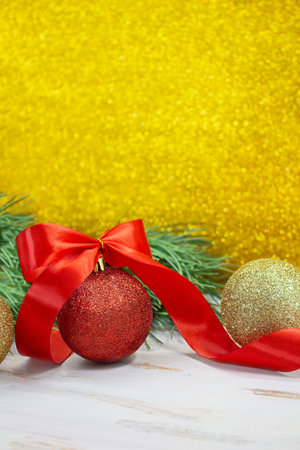 Shiny red and gold balls with bow and twisted ribbon at back of spruce branch. Yellow blurred glitter vertical background. Christmas, New Year. copy spaceの写真素材
