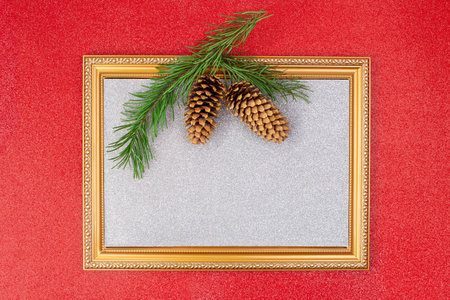 On red shiny background, golden frame with sparkling silver backdrop with spruce branch and cones. Christmas, New Year. copy spaceの写真素材
