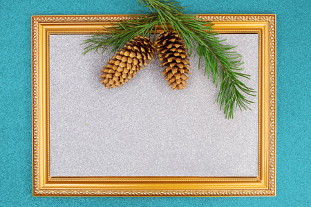 Golden frame with sparkling silver backdrop with spruce branch and cones on blue shiny background. Christmas, New Year. copy spaceの写真素材