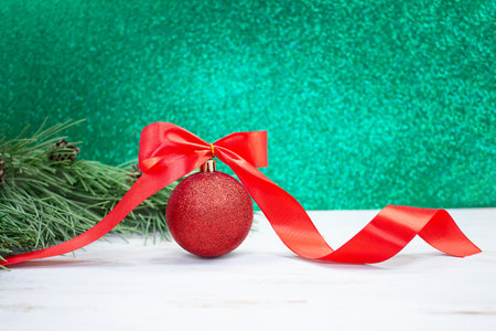 Christmas ball with red bow and twisted ribbon with spruce branches. Behind blurred green background. new year. copy spaceの写真素材