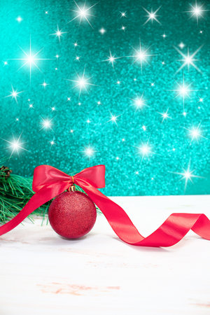 Christmas ball with pink bow and curled ribbon with spruce branches. Behind blurred green-blue background with stars. new year. vertical. copy spaceの写真素材
