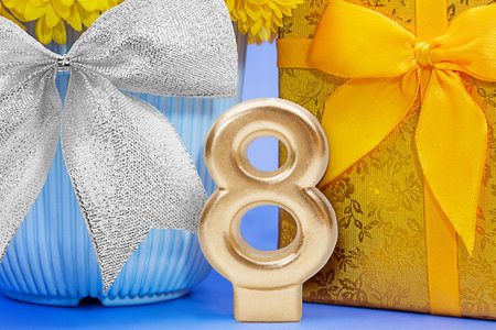 Golden number 8 with shiny yellow gift box and flower in blue pot and silver bow. International...